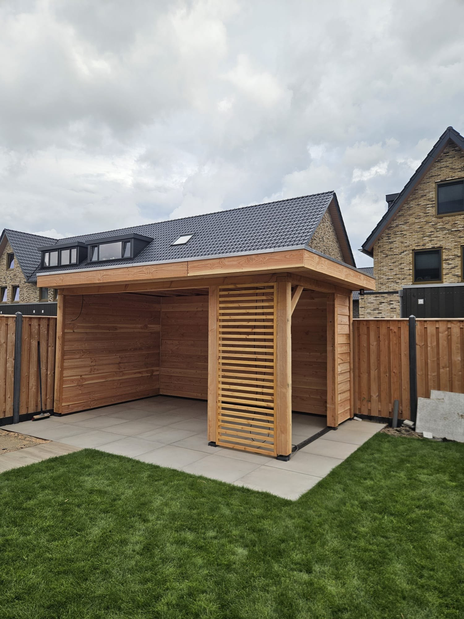 Op maat gebouwde houten overkapping met lamellenwand in een tuin in Noord-Holland